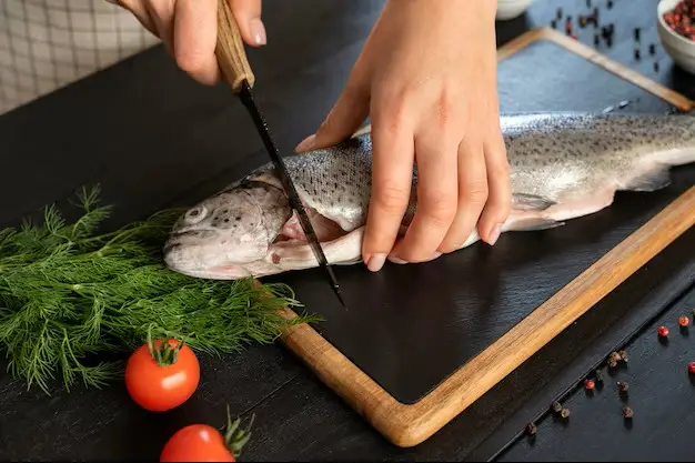 Mains préparant un poisson sur une planche avec ustensiles de cuisine